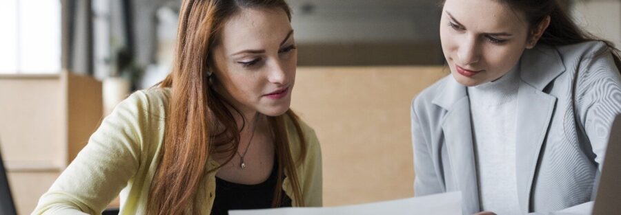 Duas mulheres sentadas, avaliando um documento. Uma delas é uma consultora de outplacement em SP. A outra é a contratante, que passa pelo processo de outplacement em SP