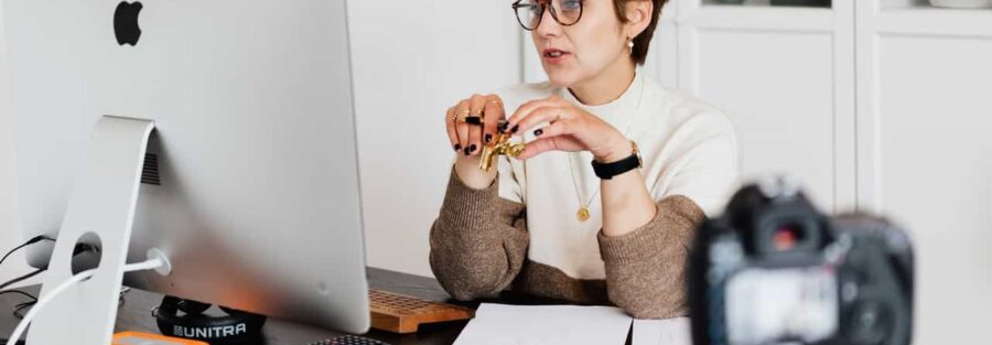 Foto de uma mulher sentada em frente a um computador e a uma câmera para ilustrar artigo sobre consultoria de recolocação profissional.