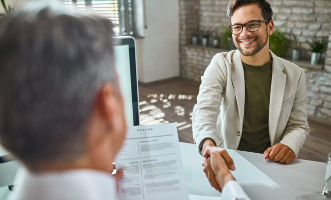 Imagem de dois homens apertando as mãos durante uma entrevista de emprego para ilustrar artigo sobre recolocação no mercado de trabalho. Foto: Freepik